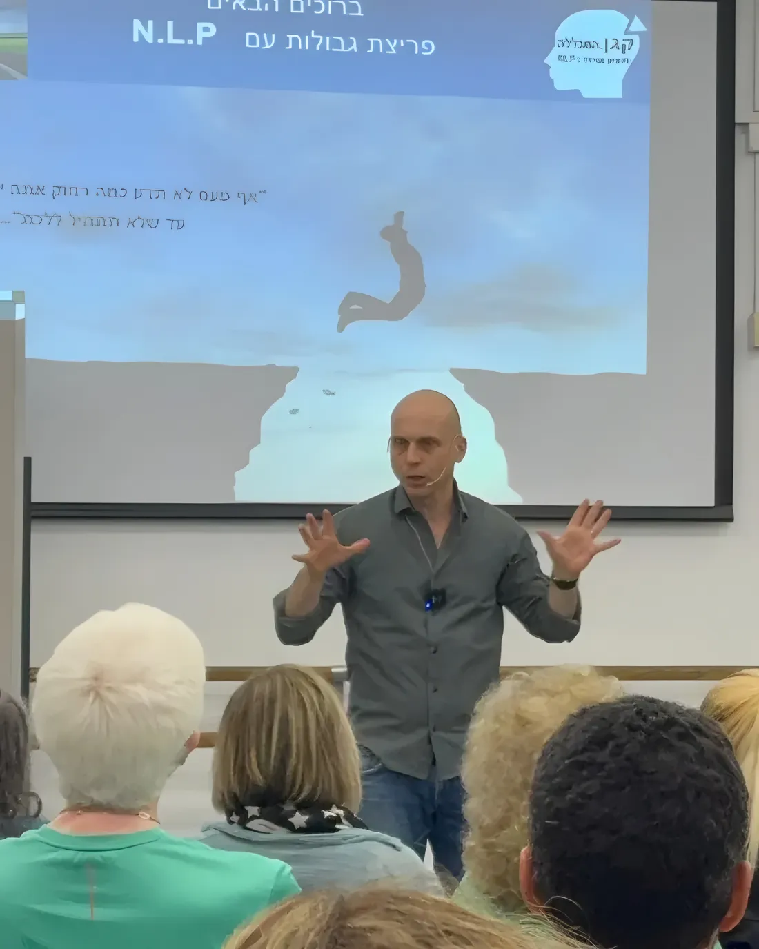 אריה קגן מלמד בסדנה. על המסך מאחוריו איור של אדם שקופץ מעל תהום